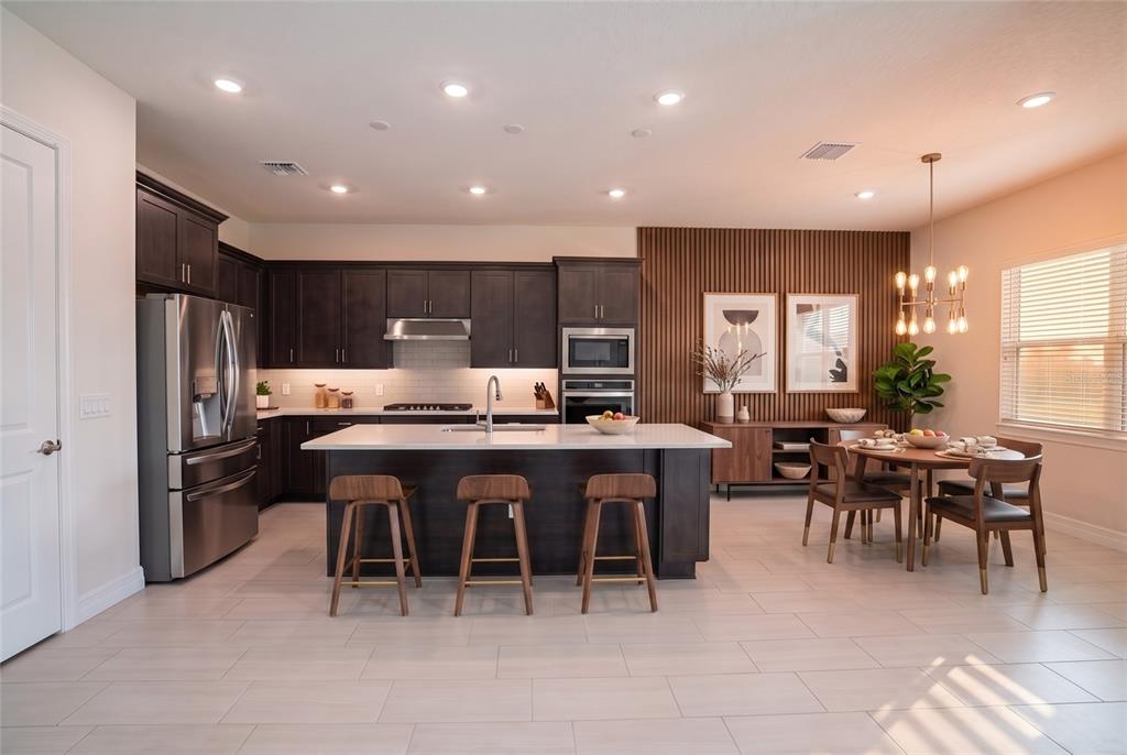 A modern kitchen features dark wood cabinetry, a central island with barstools, and a dining area — 8087 FENTON STREET, ORLANDO, FL