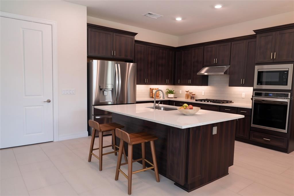 A kitchen features dark wood cabinets, a white quartz island with two stools, and stainless appliances — 8087 FENTON STREET, ORLANDO, FL