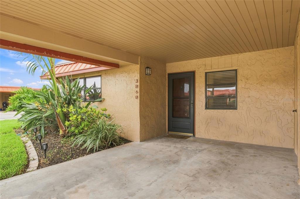 A covered concrete entryway features a dark front door, a window, and a landscaped garden — 3868 CATALINA DRIVE, BRADENTON, FL