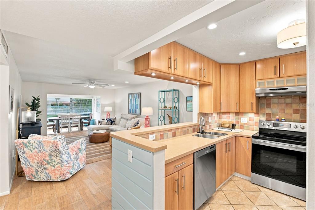 A kitchen with light wood cabinets and tile counters opens into a living and dining area — 3868 CATALINA DRIVE, BRADENTON, FL