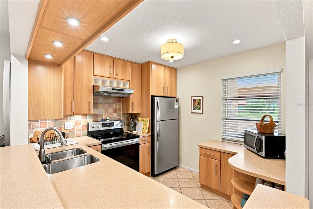 A kitchen features light wood cabinets, stainless steel appliances, a double sink, and tiled flooring — 3868 CATALINA DRIVE, BRADENTON, FL