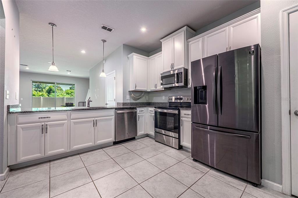 A kitchen features white cabinets, stainless steel appliances, granite countertops, and light-colored tile flooring — 3084 INLET BREEZE WAY, HOLIDAY, FL