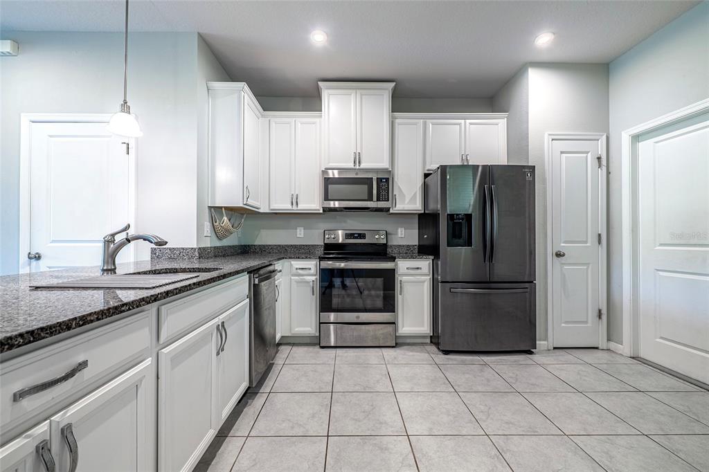 A kitchen features white cabinets, granite countertops, stainless steel appliances, and light-colored tile flooring — 3084 INLET BREEZE WAY, HOLIDAY, FL