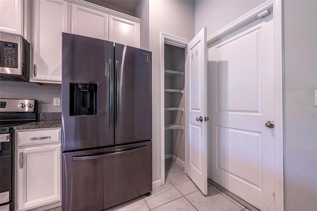 A kitchen features white cabinets, a stainless steel refrigerator, and an open pantry door — 3084 INLET BREEZE WAY, HOLIDAY, FL
