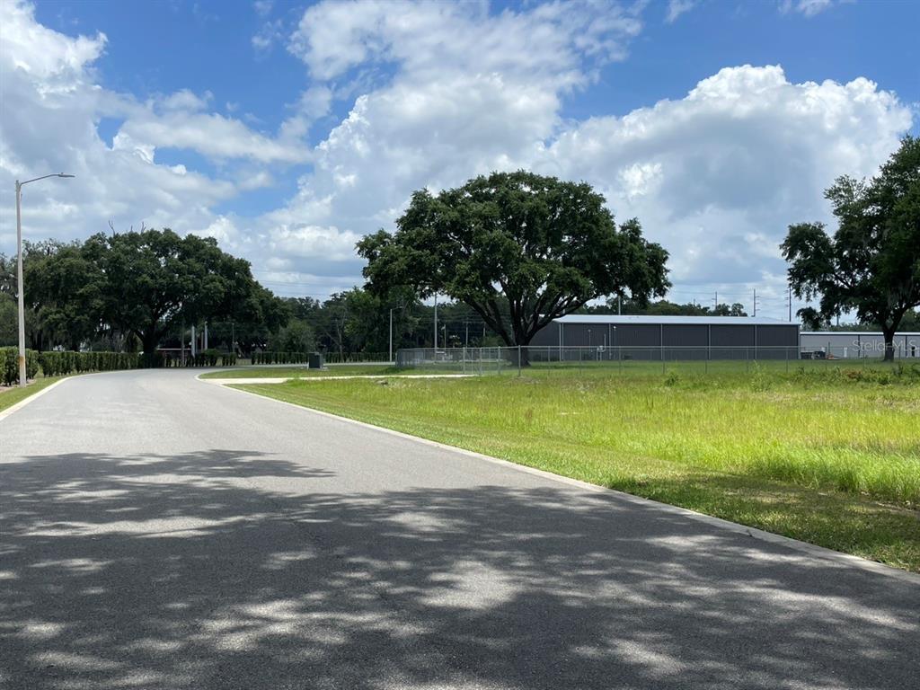 A paved road curves past a grassy lot with large trees and a metal building — 1020 DUCK BOX ROAD, UMATILLA, FL