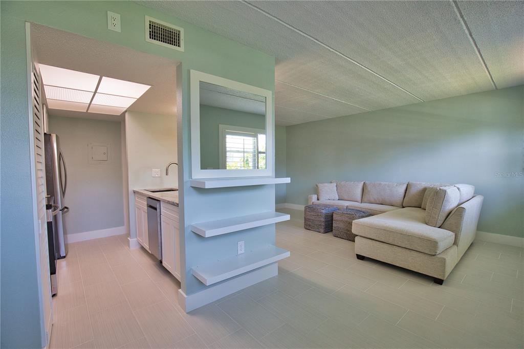 A light-colored living room features a sectional sofa, tile flooring, and an open kitchen area — 902 GIBBS ROAD UNIT 184, VENICE, FL
