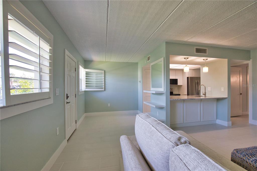 A living room with light blue walls, tile flooring, and an open kitchen with white cabinets — 902 GIBBS ROAD UNIT 184, VENICE, FL