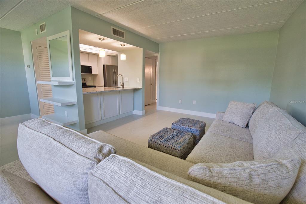 A living room with a sectional sofa faces an open kitchen with white cabinetry — 902 GIBBS ROAD UNIT 184, VENICE, FL