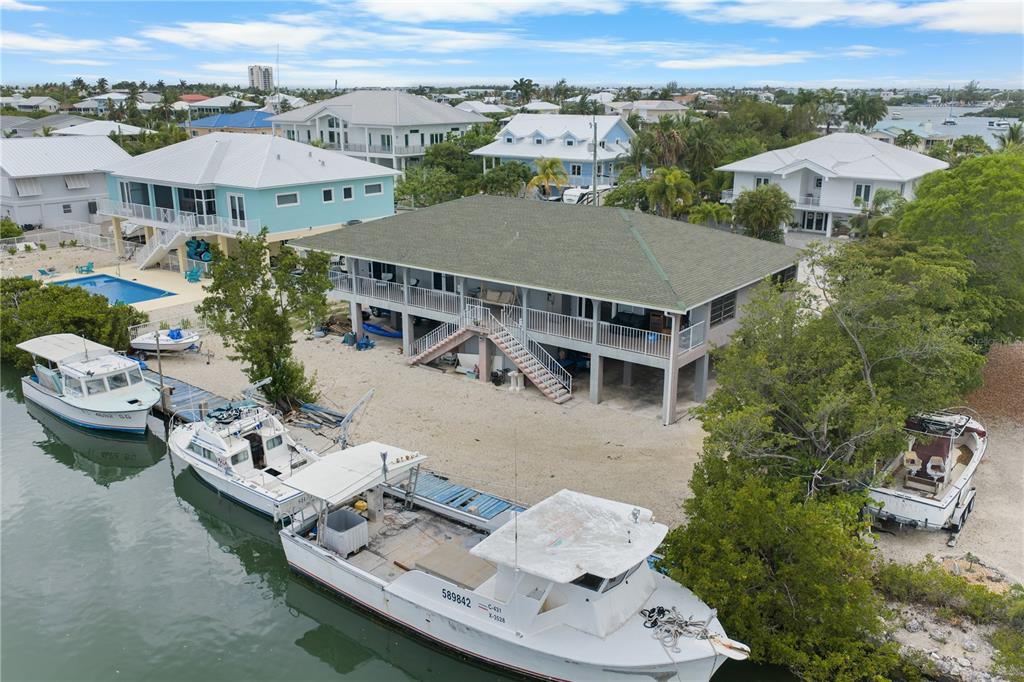 An elevated house with a green roof sits on a waterfront lot with several boats — 2100 AVENUE H, MARATHON, FL