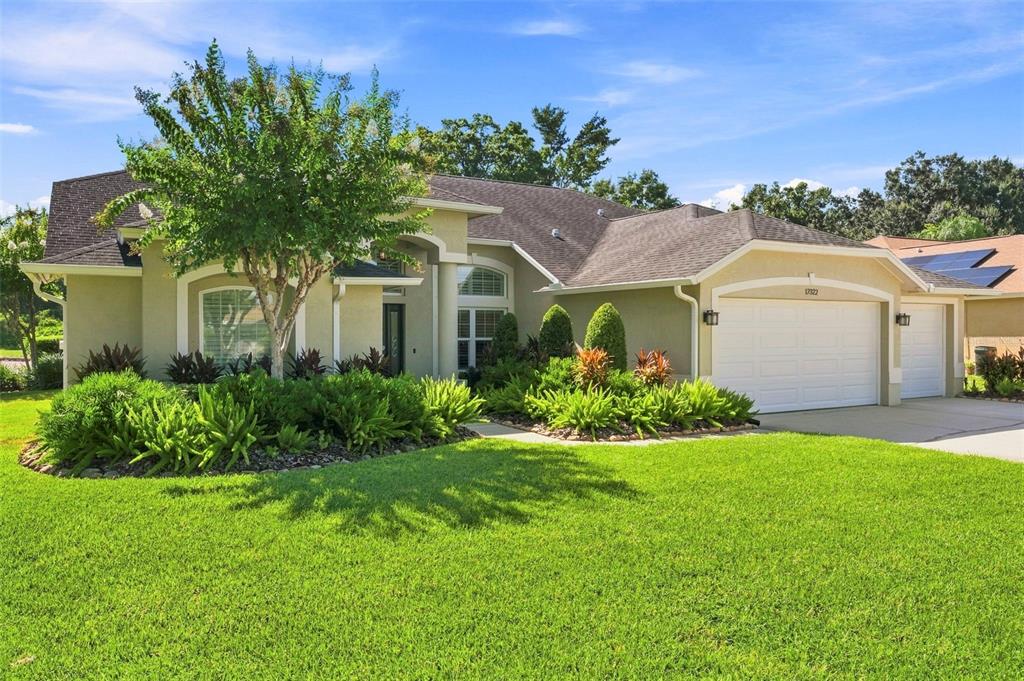 A single-story house with a white garage, tan stucco exterior, and a landscaped front yard — 17322 HUBERS COURT, ODESSA, FL