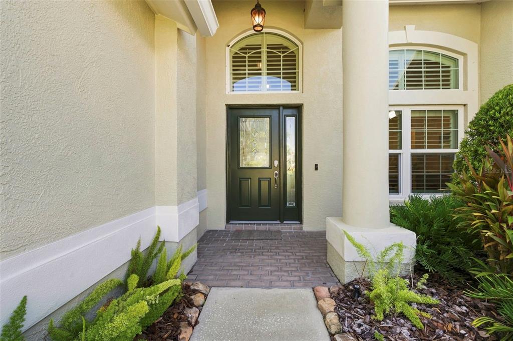 A front entryway features a dark green door with a glass insert and brick flooring — 17322 HUBERS COURT, ODESSA, FL