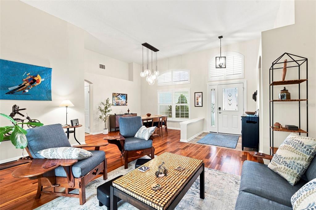 A living room with hardwood floors, blue armchairs, a coffee table, and a dining area — 17322 HUBERS COURT, ODESSA, FL
