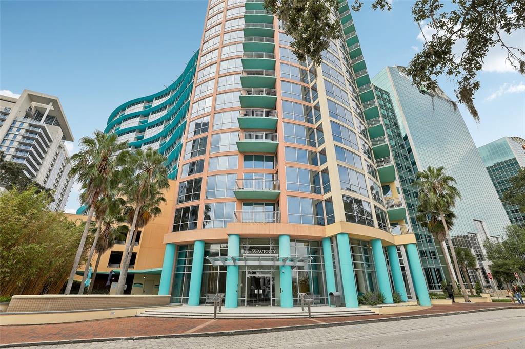 A low-angle view of a modern high-rise apartment building with teal accents and palm trees — 322 E CENTRAL BOULEVARD UNIT 806, ORLANDO, FL