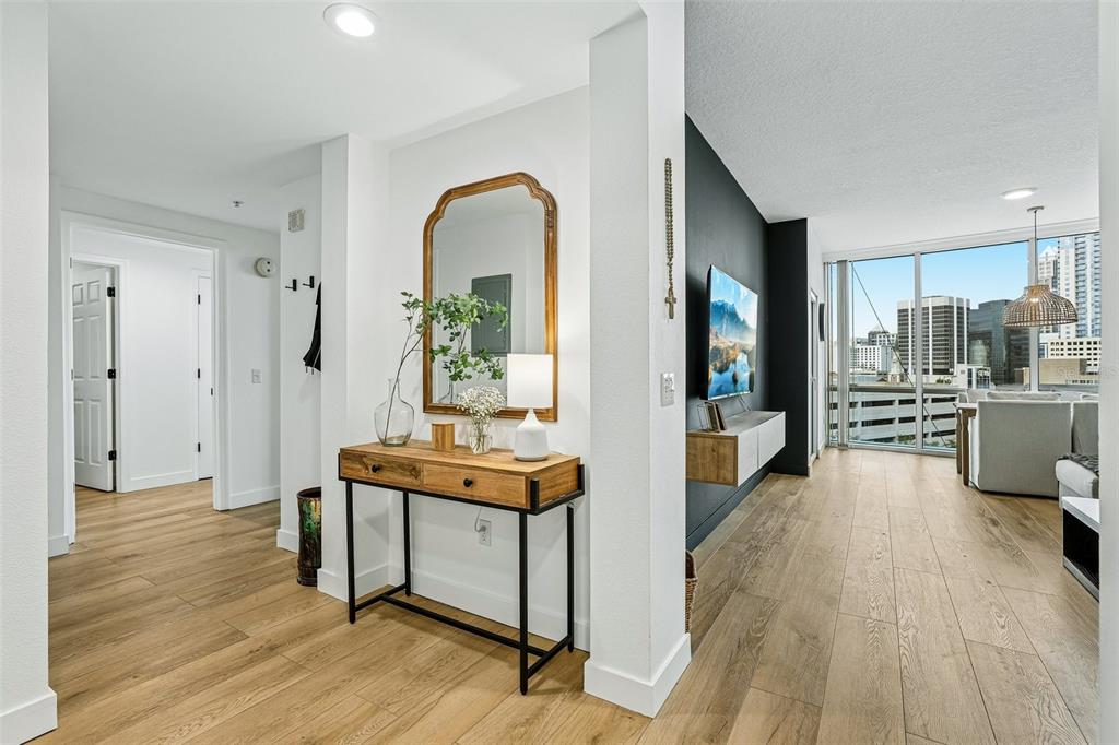 A modern entryway features a wooden console table with a mirror, leading into a living area — 322 E CENTRAL BOULEVARD UNIT 806, ORLANDO, FL