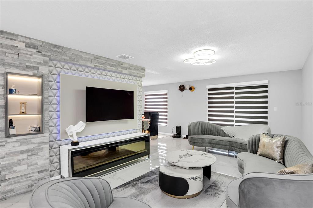 A modern living room features a stone accent wall, a fireplace, and gray velvet furniture — 5316 JADE STREET, KISSIMMEE, FL