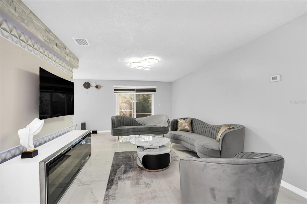 A modern living room features grey velvet curved sofas, a marble coffee table, and tile flooring — 5316 JADE STREET, KISSIMMEE, FL