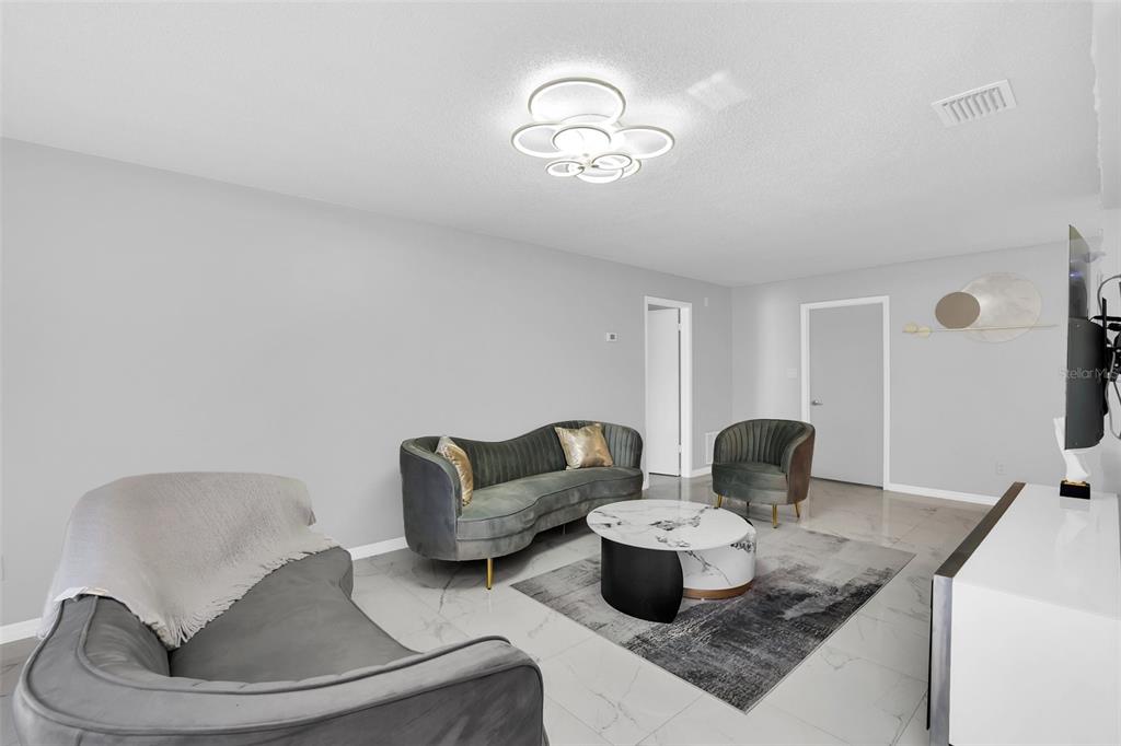 A modern living room features gray velvet furniture, a marble coffee table, and tile flooring — 5316 JADE STREET, KISSIMMEE, FL