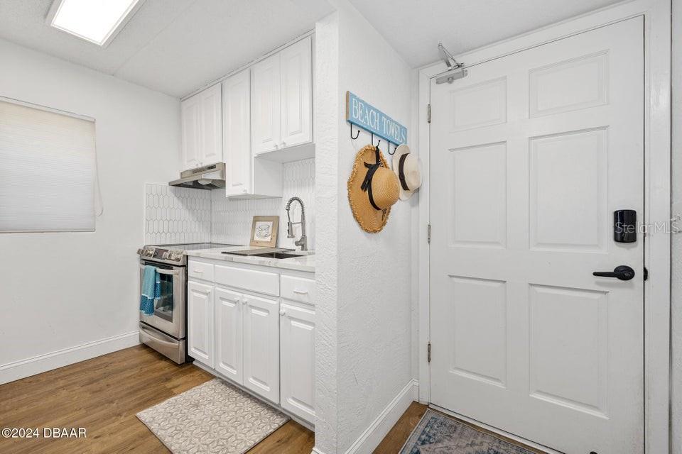 A small kitchen features white cabinetry, stainless steel appliances, and a door leading outside — 1510 OCEAN SHORE BOULEVARD UNIT 3150, ORMOND BEACH, FL
