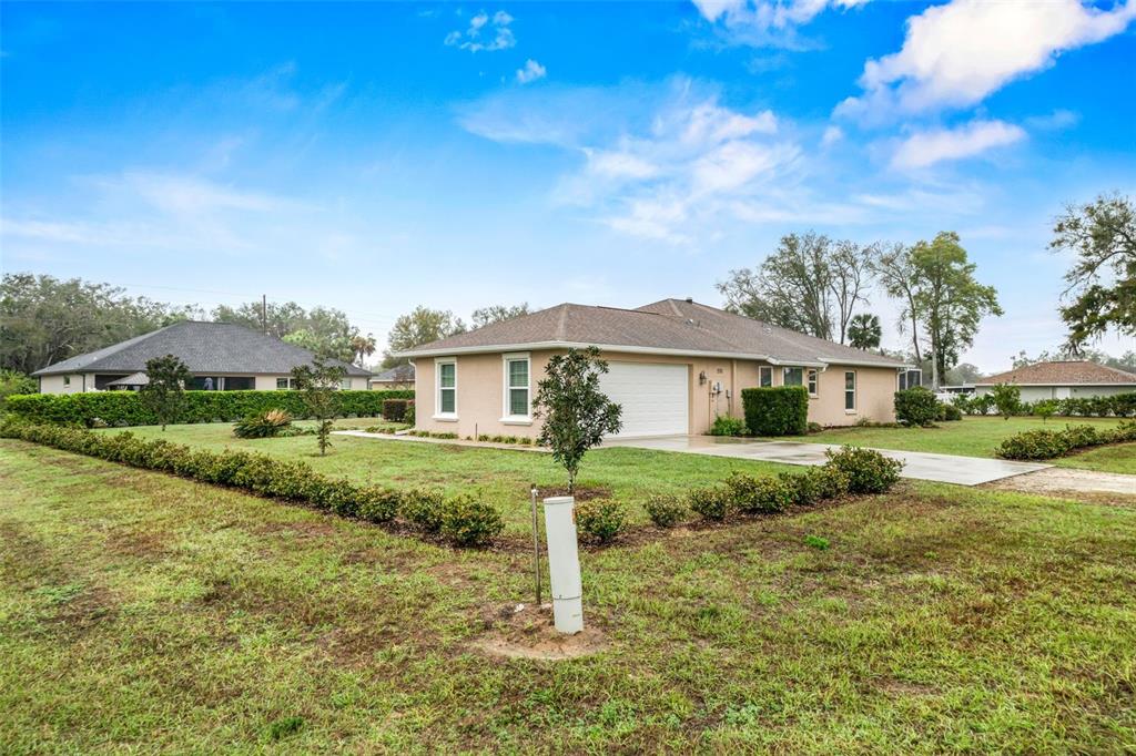 A tan single-story house with a two-car garage sits on a large grassy lot — 276 N CUNNINGHAM AVENUE, INVERNESS, FL
