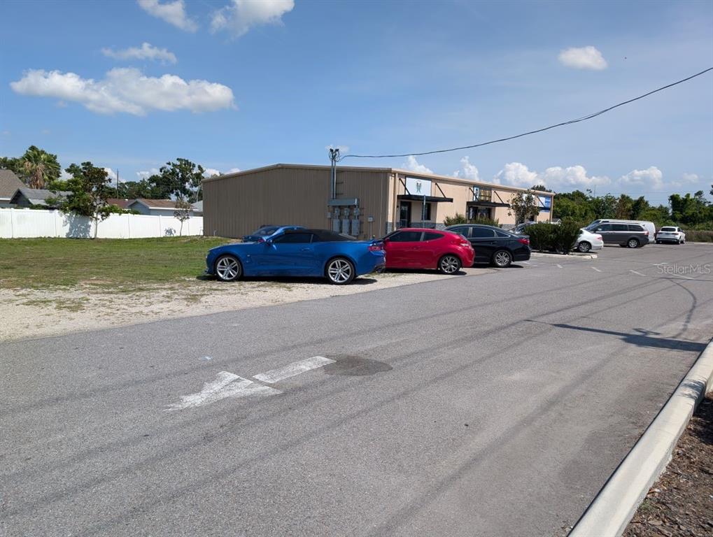 A blue sports car is parked in front of a commercial building with a parking lot — 7011 N MANHATTAN AVENUE, TAMPA, FL