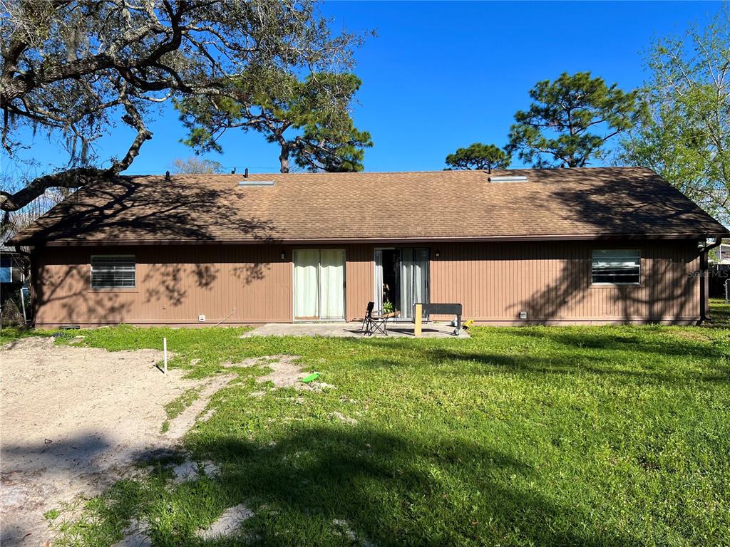 The rear exterior of a single-story house features brown siding, a shingled roof, and sliding doors — 1820 CENTRAL PARK AVENUE, ORLANDO, FL