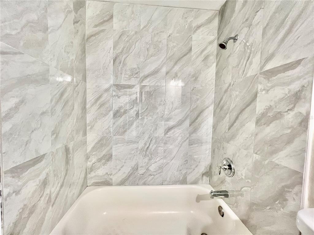 A white bathtub with a shower head and grey marble-patterned tile walls — 1820 CENTRAL PARK AVENUE, ORLANDO, FL