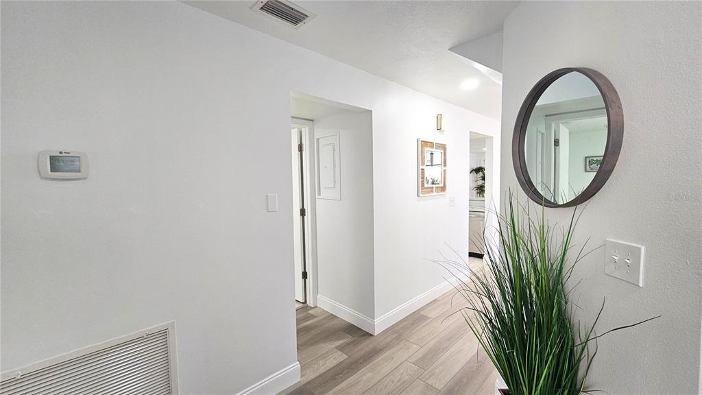 A bright hallway features white walls, light wood-look flooring, a round mirror, and a plant — 9100 PARK BOULEVARD UNIT 1, SEMINOLE, FL