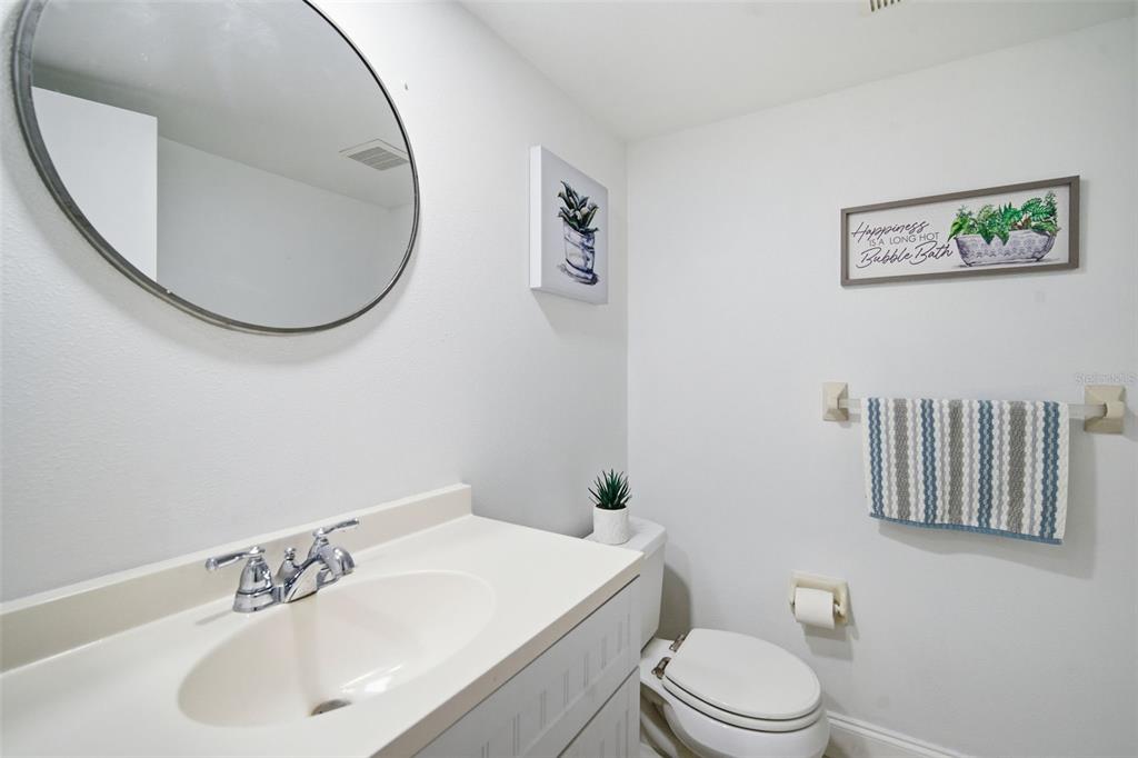 A bathroom features a white vanity, a round mirror, a toilet, and wall decor — 9100 PARK BOULEVARD UNIT 1, SEMINOLE, FL