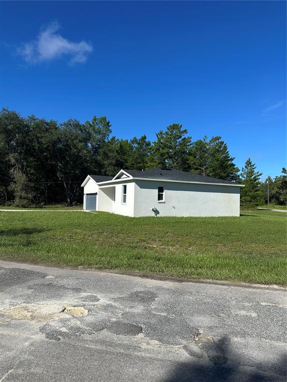 A white stucco house sits on a grassy lot bordered by a dense forest — 14 FISHER COURT, OCKLAWAHA, FL