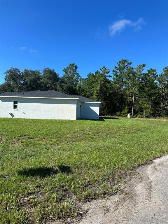 A grassy vacant lot sits at a street corner bordered by a line of trees — 14 FISHER COURT, OCKLAWAHA, FL