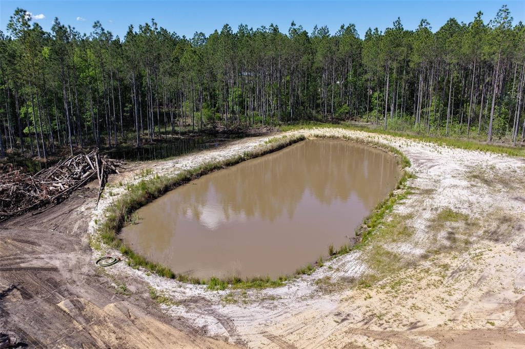 An aerial view shows a muddy pond surrounded by cleared land and a dense forest — 15539 COUNTY RD 305, BUNNELL, FL