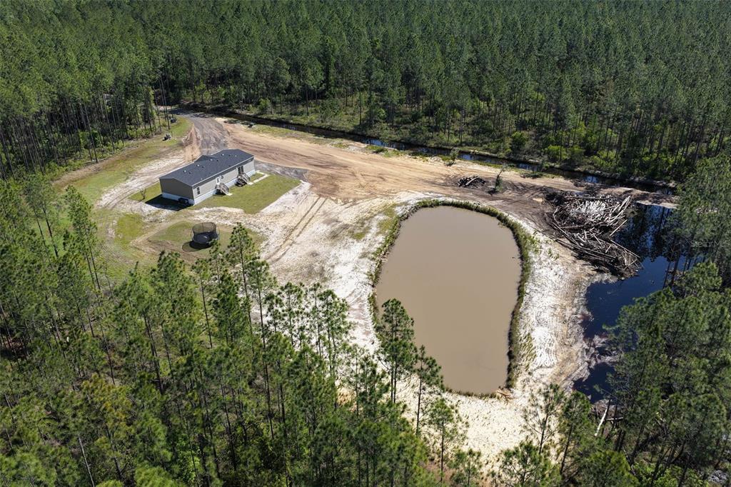 An aerial view shows a manufactured home, a pond, and a dirt driveway amidst pine trees — 15539 COUNTY RD 305, BUNNELL, FL