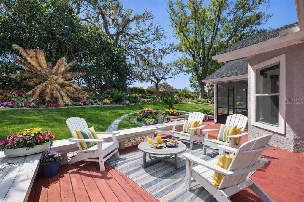 A red wooden deck features white Adirondack chairs, a round table, and a landscaped backyard — 108 OAK VIEW CIRCLE, LAKE MARY, FL
