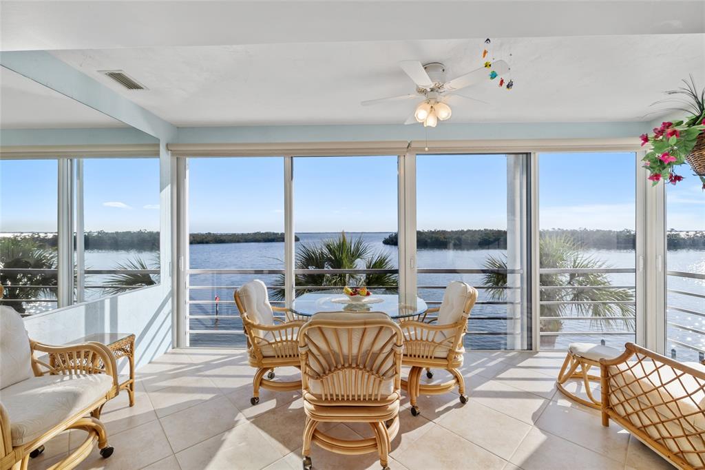 A sunroom features tile flooring, wicker furniture, and large windows overlooking a body of water — 4310 FALMOUTH DRIVE UNIT 307, LONGBOAT KEY, FL