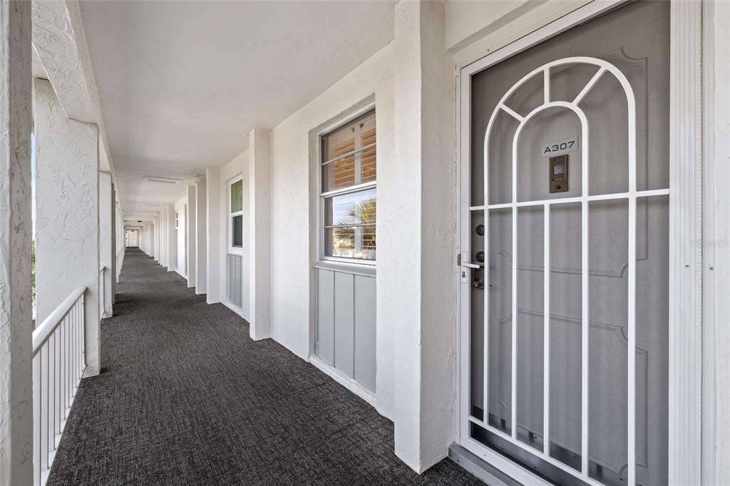 An outdoor apartment corridor features gray carpeting, white walls, and a white security screen door — 4310 FALMOUTH DRIVE UNIT 307, LONGBOAT KEY, FL
