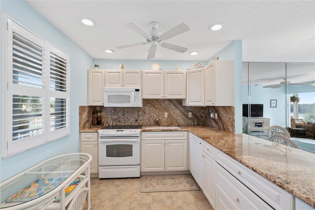 A kitchen with white cabinets, granite countertops, and a white stove in a light-blue room — 4310 FALMOUTH DRIVE UNIT 307, LONGBOAT KEY, FL