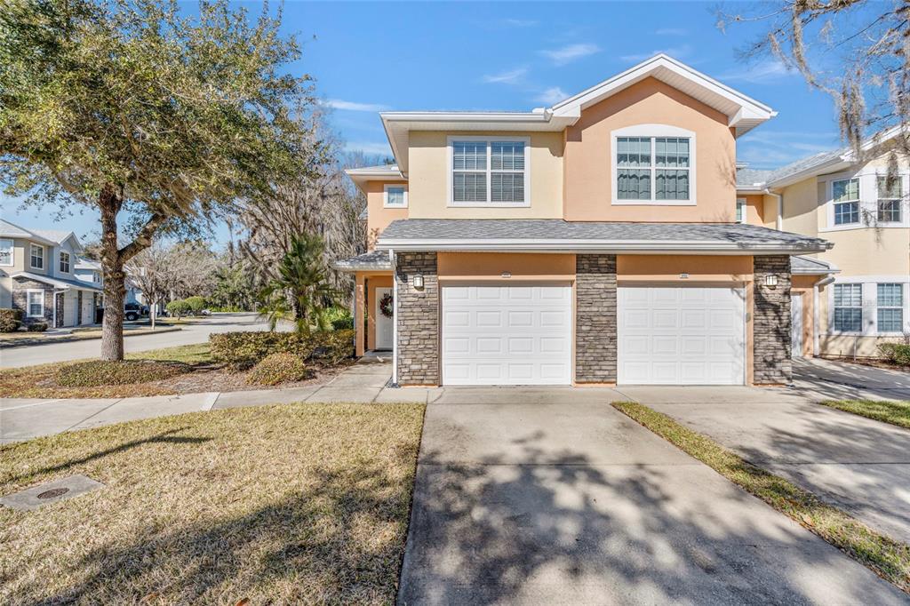 A two-story townhouse with a stone facade, two white garage doors, and a concrete driveway — 110 MAGNOLIA CROSSING POINT UNIT 1901, ST AUGUSTINE, FL