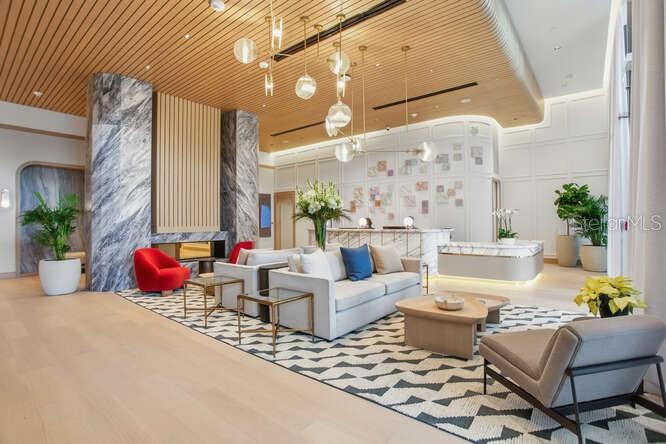 A modern lobby features a seating area with light-colored sofas, a red chair, and marble accents — 3015 S YSABELLA AVENUE UNIT 601, TAMPA, FL