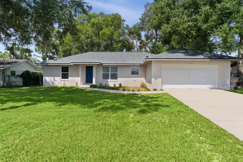 A single-story house with a light-colored exterior, a blue front door, and a two-car garage — 36127 PINE TREE STREET, FRUITLAND PARK, FL