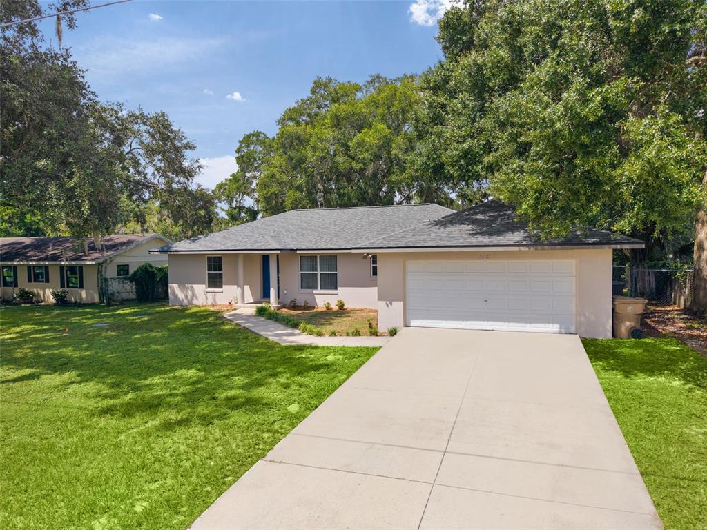 A single-story house with a light-colored exterior, a gray shingled roof, and a concrete driveway — 36127 PINE TREE STREET, FRUITLAND PARK, FL