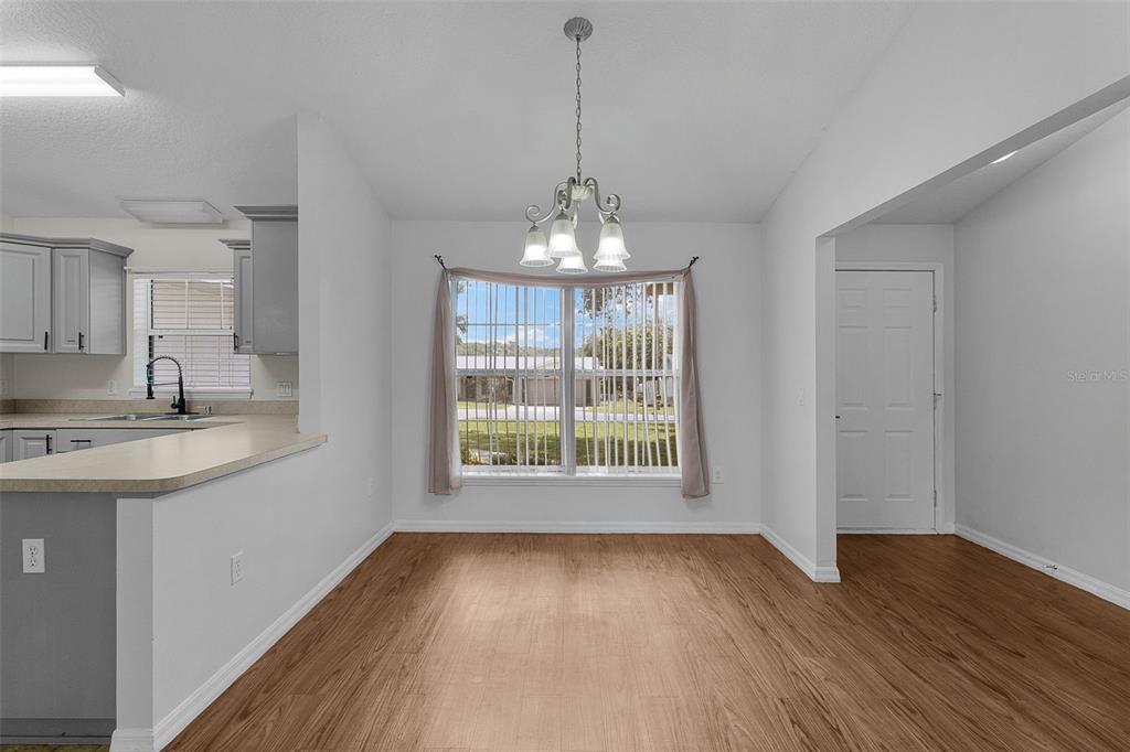 A dining area features light wood-look flooring, a central chandelier, and a large bay window — 36127 PINE TREE STREET, FRUITLAND PARK, FL