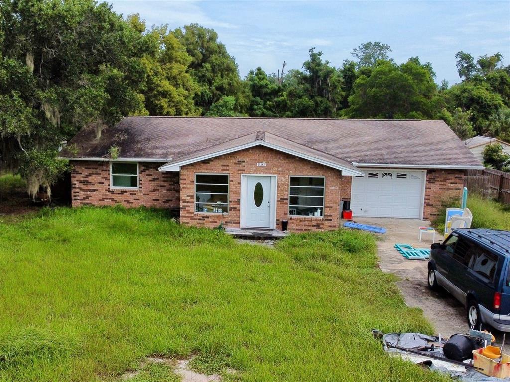 A single-story brick house with a front-facing garage and an overgrown lawn — 5243 EAGLES NEST ROAD, FRUITLAND PARK, FL