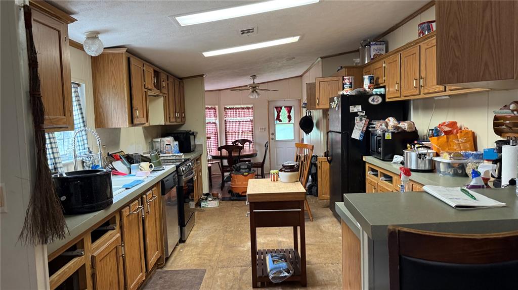 A kitchen with wood cabinets, laminate countertops, and a dining area in the background — 12171 NW 168TH PLACE, REDDICK, FL