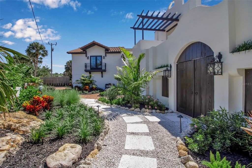 A gravel path with stone pavers leads to a white building with a wooden arched door — 121 N CASEY KEY ROAD, OSPREY, FL