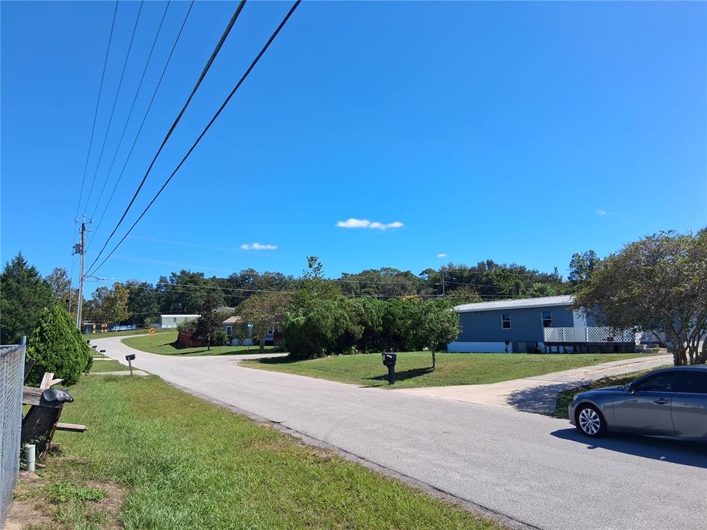 A paved road winds past a blue mobile home and a parked gray car — 6290 SE 140TH PLACE, SUMMERFIELD, FL