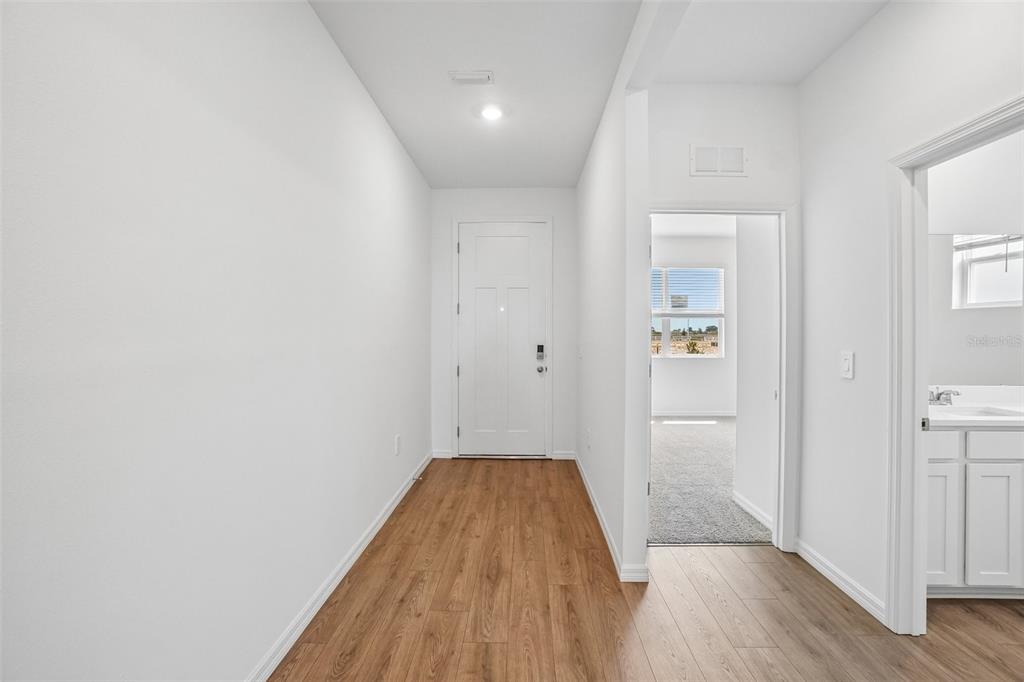 A bright entryway with wood-look flooring leads to a front door and interior rooms — 5375 CLOUDBERRY AVENUE, LAKELAND, FL