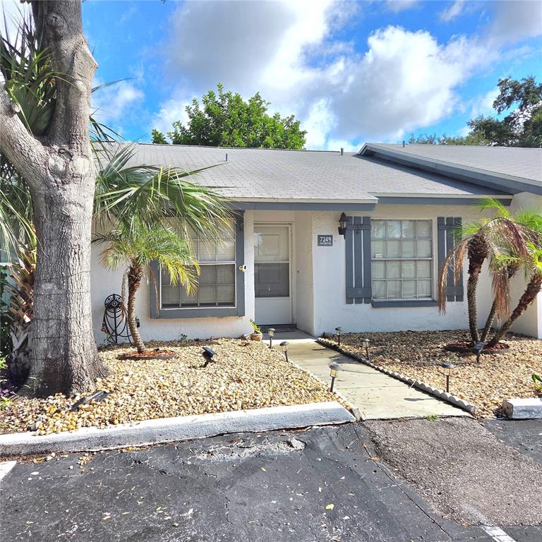 A single-story house exterior features a white facade, gray shutters, and a gravel front yard — 7249 PARKSIDE VILLAS DRIVE N, ST PETERSBURG, FL