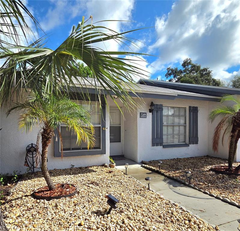 A single-story house exterior features a palm tree, gravel landscaping, and a concrete walkway — 7249 PARKSIDE VILLAS DRIVE N, ST PETERSBURG, FL