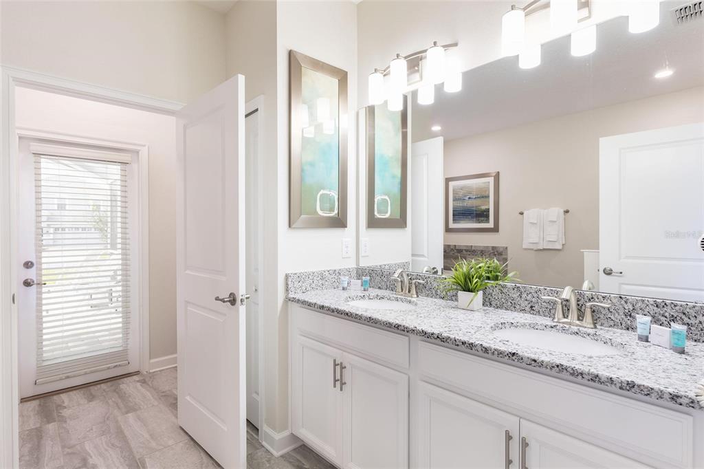 A bathroom with a double vanity, granite countertops, white cabinets, and a glass-paned exterior door — 9045 STINGER DRIVE, DAVENPORT, FL