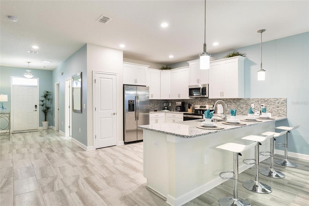 A kitchen features white cabinets, granite countertops, a stainless steel refrigerator, and a breakfast bar — 9045 STINGER DRIVE, DAVENPORT, FL